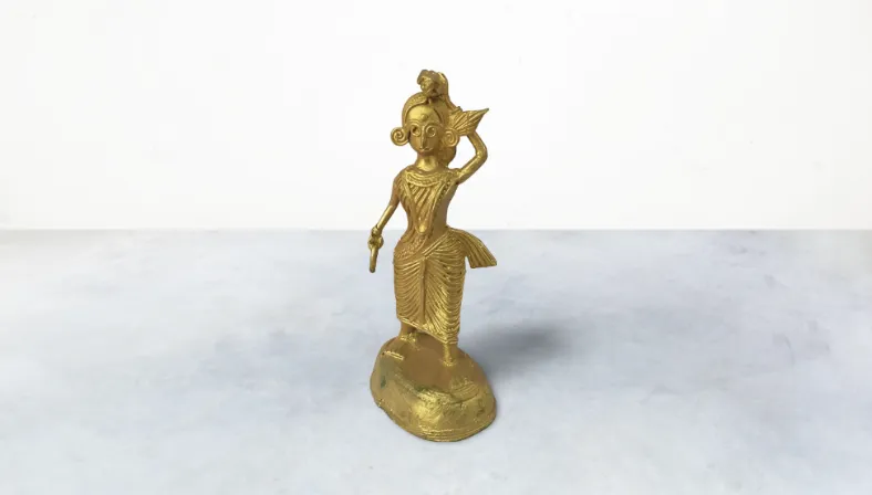This charming Dokra art piece portrays a girl character with authentic craftsmanship using the traditional metal casting technique. Each detail is meticulously crafted, showcasing the artistry and cultural richness of India. The girl is depicted in a pose that exudes grace and innocence, capturing the essence of traditional aesthetics. Perfect for collectors and art enthusiasts alike, this figurine adds a touch of cultural elegance to any space. Whether displayed on a shelf, desk, or as a centerpiece, it serves as a reminder of India's artistic heritage and timeless craftsmanship. Elevate your decor with this unique Dokra masterpiece, celebrating the beauty of handmade art.